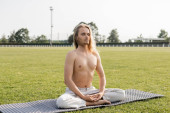 shirtless and long haired man meditating in easy pose with closed eyes on yoga mat on grassy outdoor stadium Tank Top #648519248