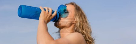 junger langhaariger Yoga-Mann trinkt erfrischendes Wasser aus Sportflasche vor blauem Himmel, Banner