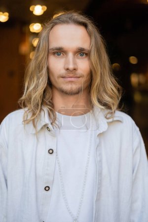 portrait d'un homme de yoga aux cheveux blonds en chemise blanche regardant la caméra avec la ville floue sur le fond 