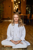 carefree man with closed eyes and long fair hair meditating in easy pose in house t-shirt #648522704
