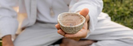 cropped view of blurred man holding ceramic bowl with tea outdoors, banner