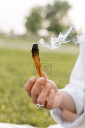 Téléchargez les photos : Foyer sélectif de palo santo fumant bâton dans la main de l'homme de yoga cultivé - en image libre de droit