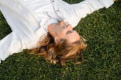 top view of carefree long haired man in white shirt lying and smiling on green lawn puzzle #648523884