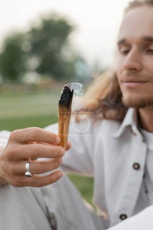 palo aromático ardiente en la mano del hombre borroso meditando al aire libre