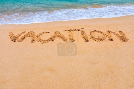 Urlaubstext am Strand. Urlaub an einem tropischen Sandstrand. "Urlaub" steht in den Sand am Strand geschrieben, im Hintergrund blaue Wellen. Urlaub am Sandstrand-Konzept.