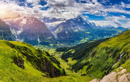 Panoramic view of idyllic mountain scenery in the Alps with fresh green meadows in bloom on a beautiful sunny day in summer, Switzerland. Idyllic mountain landscape in the Alps with meadows in summer.