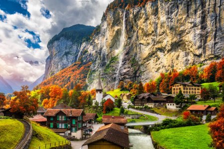 Vue d'automne captivante sur la vallée de Lauterbrunnen avec une magnifique cascade de Staubbach et les Alpes suisses au coucher du soleil. Lauterbrunnen village avec feuillage rouge d'automne, Oberland Berner, Suisse, Europe.