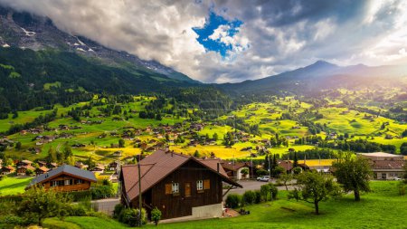 Foto de Grindelwald pueblo vista y verano Alpes suizos montañas panorama paisaje, chalets de madera en campos verdes y altos picos de fondo, Suiza, Bernese Oberland, Europa. - Imagen libre de derechos