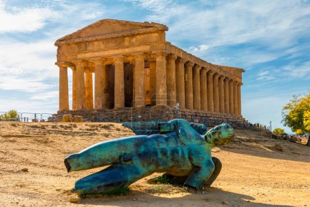 Bronze statue of Icarus in front of the Temple of Concordia at the Valley of the Temples. Temple of Concordia and the statue of Fallen Icarus, in the Valley of the Temples, Agrigento, Sicily, Italy.