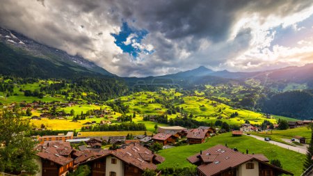 Foto de Grindelwald pueblo vista y verano Alpes suizos montañas panorama paisaje, chalets de madera en campos verdes y altos picos de fondo, Suiza, Bernese Oberland, Europa. - Imagen libre de derechos