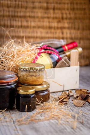 Photo for A vertical shot of a wooden gift crate with bottles of wine and straw near jars of homemade products - Royalty Free Image