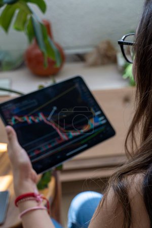 Téléchargez les photos : Un plan vertical d'une jeune femme trading crypto devises en ligne et les actions avec sa tablette - en image libre de droit