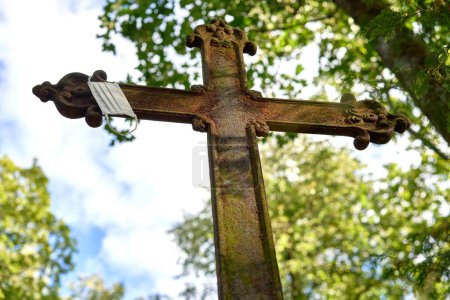 Téléchargez les photos : Plan en angle bas d'une croix de métal rouillée avec un masque accroché dessus dans un vieux cimetière - en image libre de droit