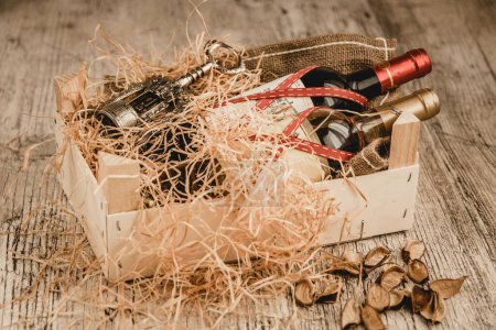 Photo for A closeup shot of a wooden gift crate with bottles of wine, a wine opener, and decorative straw - Royalty Free Image