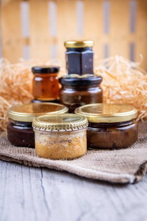 Photo for A vertical shot of jars of homemade cooking products like jams and sauces near the decorative straw - Royalty Free Image