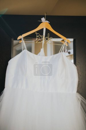 Téléchargez les photos : Un gros plan vertical de la robe blanche de la mariée accrochée à un cintre devant un miroir - en image libre de droit