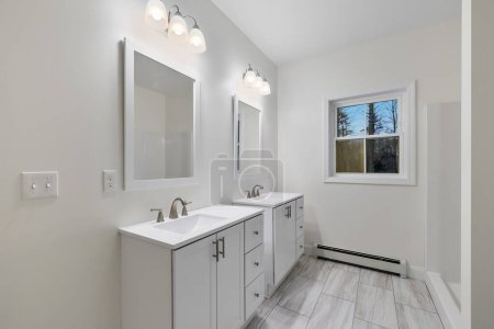 Téléchargez les photos : L'intérieur d'une salle de bain blanche avec des luminaires muraux, des éviers et des armoires et un chauffe-plinthe sous la fenêtre - en image libre de droit