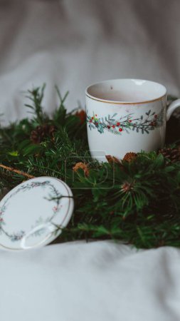 Photo for A vertical shot of a tea cup with a pine tree wreath on white fabric - Royalty Free Image