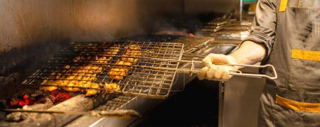 Téléchargez les photos : Un angle élevé d'une viande grillée à la main sur un fond de grillage de charbon et de fumée - en image libre de droit