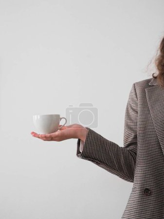 Photo for A vertical shot of a woman's hand holding a coffee cup on a grey background - Royalty Free Image