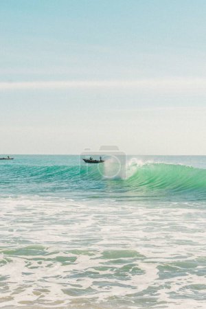 Foto de Un disparo vertical del barco en las olas espumosas cerca de la playa en un día soleado - Imagen libre de derechos