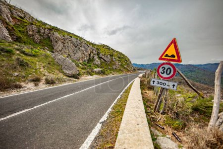 Photo for A road sign with a speed limit of 30 km per hour near a rocky hillside and under a cloudy sky - Royalty Free Image