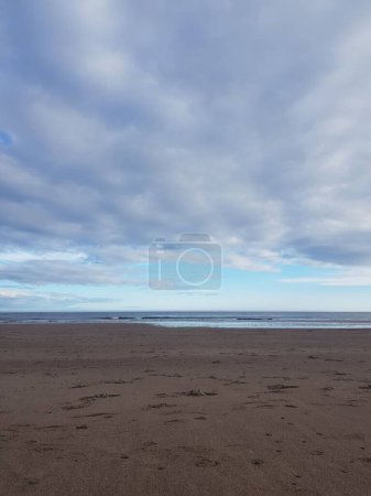 Foto de Un disparo vertical de suaves olas oceánicas en una playa de arena bajo un cielo nublado - Imagen libre de derechos