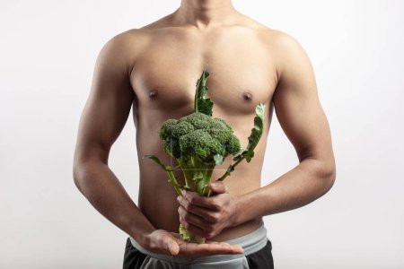 Téléchargez les photos : Le concept de peser la perte et l'alimentation, un homme torse nu sport posant avec un brocoli à la main - en image libre de droit