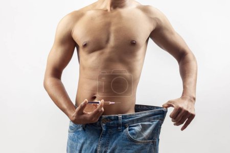 Photo for The concept of weight loss, a shirtless fitness model taking steroids injection wearing loose jeans - Royalty Free Image