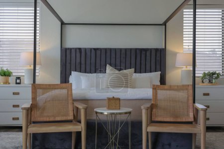 Téléchargez les photos : Une chambre moderne décorée avec deux chaises devant un lit avec des draps et des oreillers blancs et deux tables de chevet sur les côtés - en image libre de droit