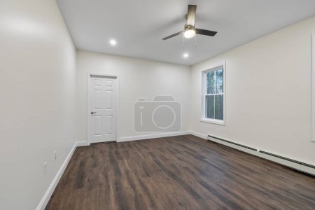 Photo for The interior of a room with a parquet floor, a baseboard heater on the white wall and a ceiling fan - Royalty Free Image
