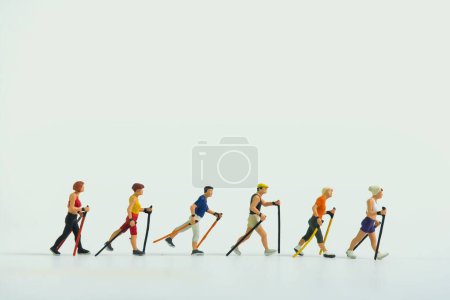Photo for The miniature figures of hikers walking holding sticks in both hands on a white background - Royalty Free Image