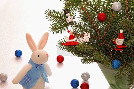 Téléchargez les photos : Peluche - un lapin sur le fond de branches d'épinette décorées de jouets anciens et de boules brillantes. - en image libre de droit