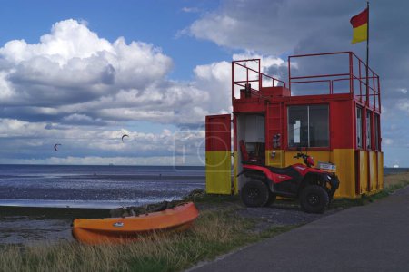 Téléchargez les photos : Des sauveteurs en service dans une cabane rouge et jaune sur la plage Dollymount Strand à Dublin, en Irlande. Les parapentes et le ciel nuageux de l'été en arrière-plan. - en image libre de droit