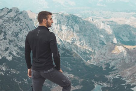 Téléchargez les photos : Un homme en noir et gris debout sur le sommet de la montagne Durmitor regardant de côté - en image libre de droit