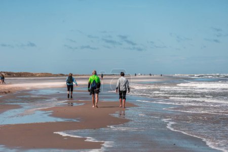 Photo for A back shot of adult people walking on the sandy beach in Skagen town on a sunny day, Denmark - Royalty Free Image
