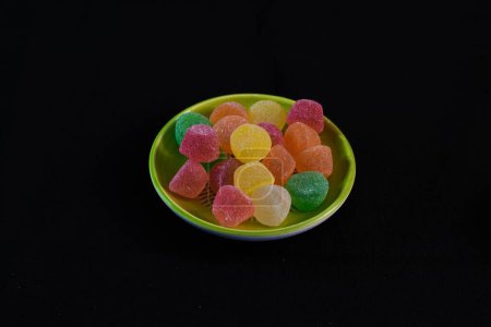 Téléchargez les photos : Les bonbons colorés sur une assiette isolée sur fond noir - en image libre de droit
