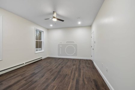 Foto de El interior de una habitación con suelo de parquet, calentador de zócalo en las paredes blancas, un ventilador de techo - Imagen libre de derechos