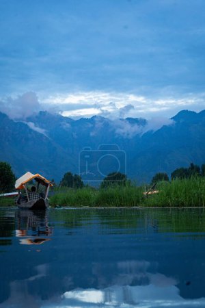 Téléchargez les photos : Un homme naviguant sur le magnifique lac Dal avec une végétation luxuriante et des montagnes couvertes de nuages spectaculaires - en image libre de droit