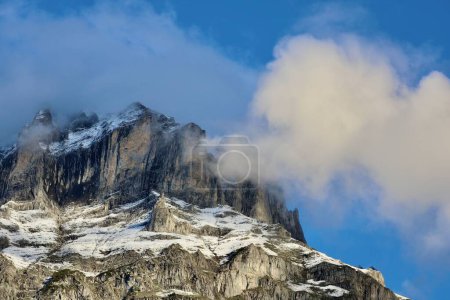 Foto de Un plano de ángulo bajo de un pico rocoso cubierto de nieve bajo las nubes y el cielo azul - Imagen libre de derechos