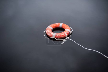 Foto de Un gran ángulo de una boya salvavidas naranja salvavidas con cuerda en la superficie del agua - Imagen libre de derechos