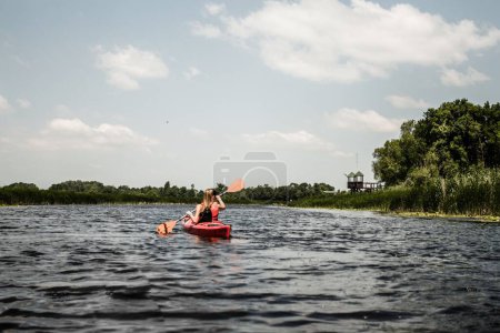 Photo for A girl kayaking in the lake with surrounding greenery on a sunny day - Royalty Free Image