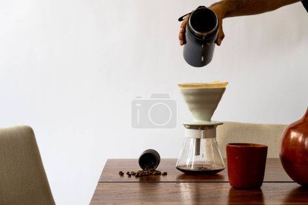 Foto de Una persona vertiendo agua en el equipo de filtro de café en una mesa de madera con granos de café - Imagen libre de derechos