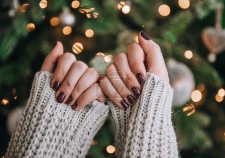 Téléchargez les photos : Gros plan des mains féminines avec des clous peints devant l'arbre de Noël avec des lumières bokeh. - en image libre de droit