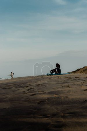 Photo for A vertical shot of a surfer resting on the beach with blue sky in the background - Royalty Free Image
