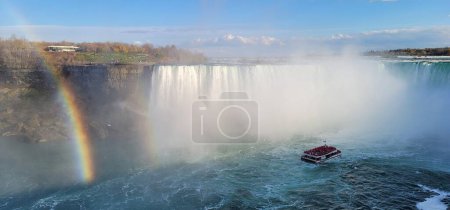 Téléchargez les photos : Un bateau touristique dans la brume de la rivière Niagara au Canada, avec les chutes Niagara et un arc-en-ciel en arrière-plan - en image libre de droit