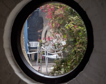 Photo for The view of a patio garden with chairs from a porthole window. - Royalty Free Image