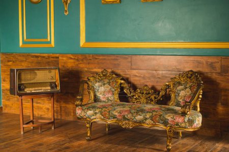 Photo for An antique baroque-style couch with a golden frame and floral patterns beside a vintage radio player - Royalty Free Image