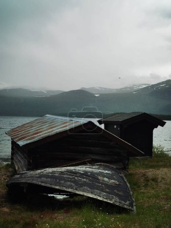 Téléchargez les photos : Un plan vertical de cabanes délabrées sur un rivage avec des montagnes et un ciel nuageux en arrière-plan - en image libre de droit