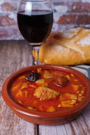 Photo for Clay casserole with Madrid-style stewed tripe, typical spanish food on a wooden table with a brick wall in the background. - Royalty Free Image